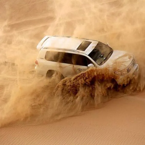 A 4x4 vehicle from The Raj Tourism navigating through the vast sand dunes during a desert safari in Dubai.